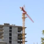 Construction site with a tall yellow crane beside a partially built concrete building against a clear blue sky