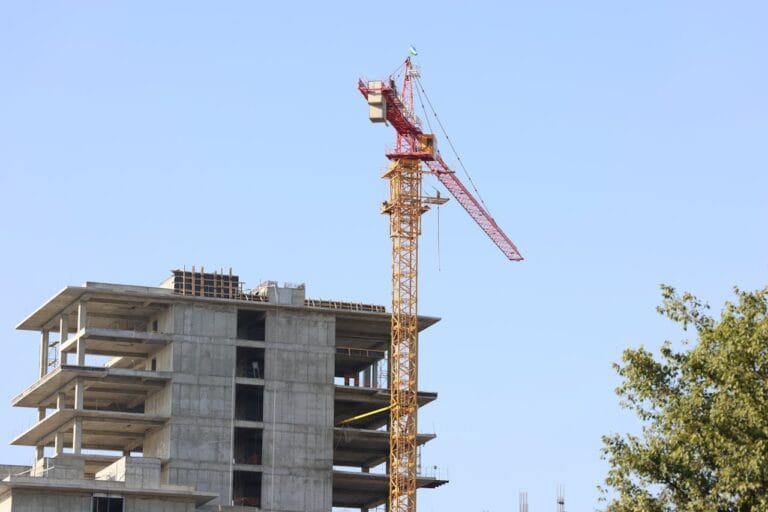 Construction site with a tall yellow crane beside a partially built concrete building against a clear blue sky
