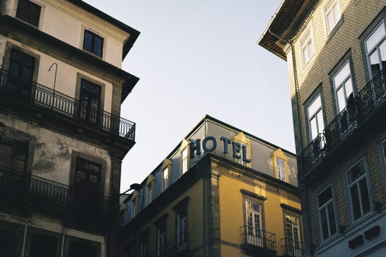 Street level view of two tall buildings facing each other with wrought iron balconies a hotel sign is visible on the corner building against a clear sky