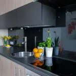 Modern kitchen with dark countertops gray cabinets and a stainless sink bowls of oranges and lemons and potted flowers on the counter