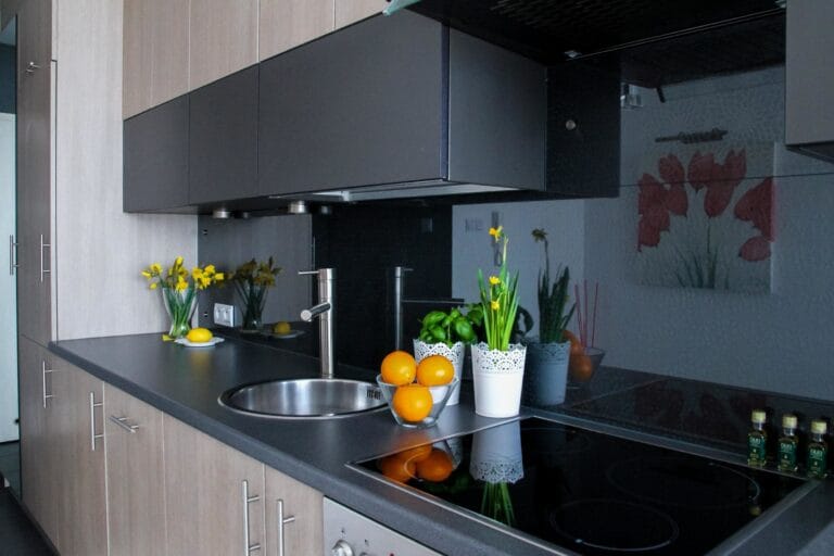Modern kitchen with dark countertops gray cabinets and a stainless sink bowls of oranges and lemons and potted flowers on the counter