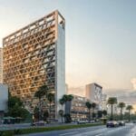 Modern urban scene featuring a large geometric lattice office building flanked by palm trees and a busy street with cars and pedestrians at duskearly evening