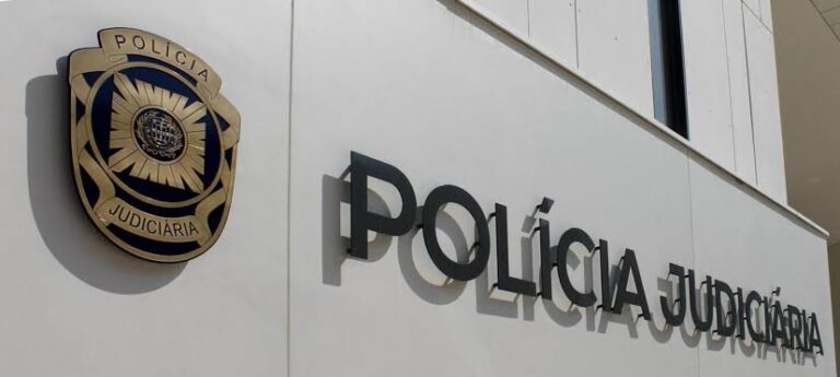 Polícia Judiciária shield badge mounted on a white wall beside the POLICIA JUDICIARIA lettering