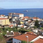Coastal town with red tiled roofs and pastel buildings overlooking the blue sea a cargo ship in the distance