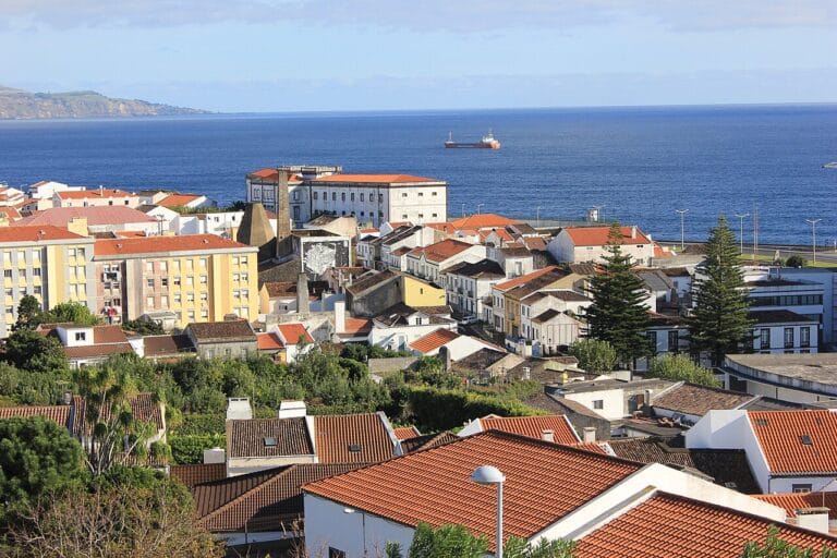Coastal town with red tiled roofs and pastel buildings overlooking the blue sea a cargo ship in the distance
