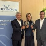 Three suited professionals toast with champagne in front of a Verlingue insurance banner that reads Protegemos o Futuro