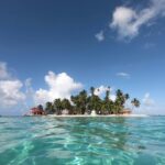 Tropical island with palm trees and thatched huts along a white sandy beach viewed from clear turquoise water