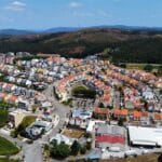 Aerial view of a circular suburban neighborhood with colorful houses arranged along concentric streets amid green hills in the background