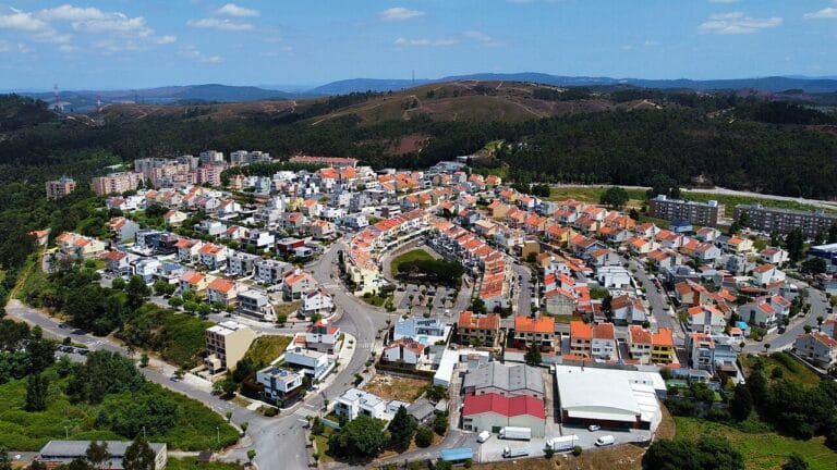 Aerial view of a circular suburban neighborhood with colorful houses arranged along concentric streets amid green hills in the background
