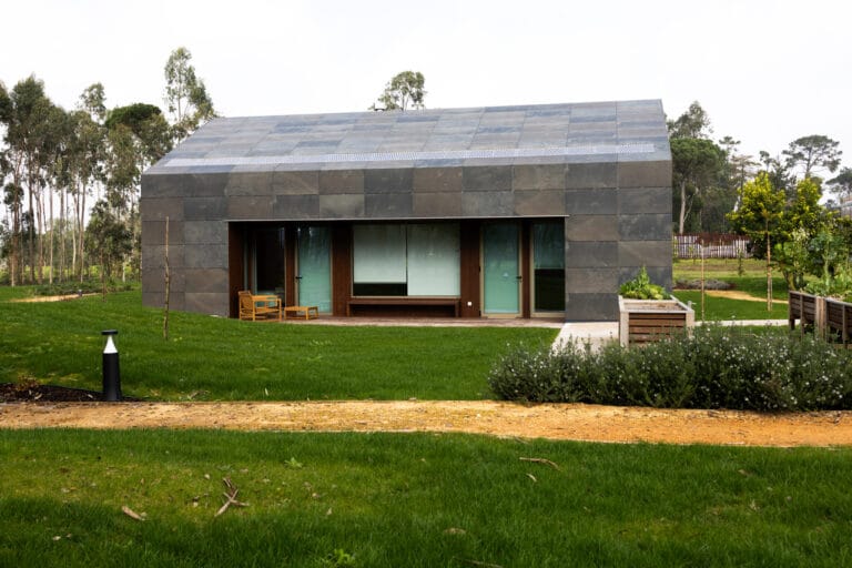 Modern single story house with dark slate exterior large sliding glass doors and a wooden porch on a green lawn