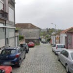 Cobblestone street in a residential area with parked cars on both sides and mixed brick buildings a worker in orange near the sidewalk