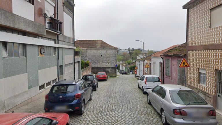Cobblestone street in a residential area with parked cars on both sides and mixed brick buildings a worker in orange near the sidewalk