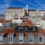 Group of people dining on a rooftop terrace with red tiled roofs and a historic building in the background