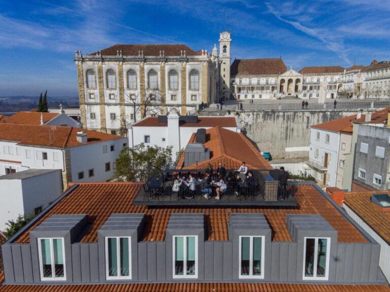 Group of people dining on a rooftop terrace with red tiled roofs and a historic building in the background