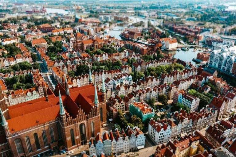 Aerial view of a European town with dense red tiled roofs a brick church in the foreground and a winding canal nearby