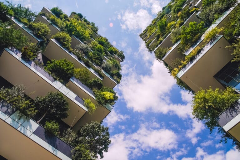 Viewed from below a modern residential building with lush greenery on each balcony against a blue sky