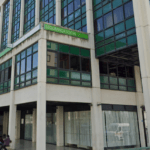 Exterior view of a government office building with green tinted windows and a Segurança Social sign people sit outside along the walkway