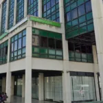 Exterior view of a government office building with green tinted windows and a Segurança Social sign people sit outside along the walkway