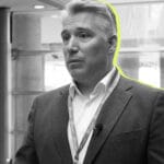 Man in a blazer with a lanyard standing in a modern office or conference space highlighted outline around him