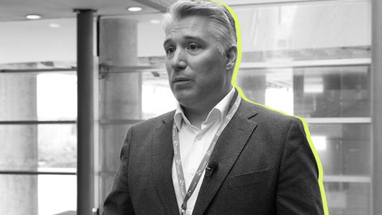 Man in a blazer with a lanyard standing in a modern office or conference space highlighted outline around him