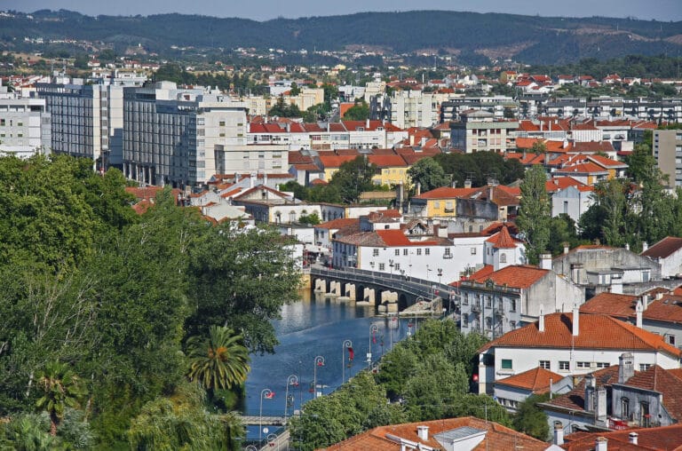 Cityscape of a riverfront town with red tiled roofs a stone bridge and distant hills