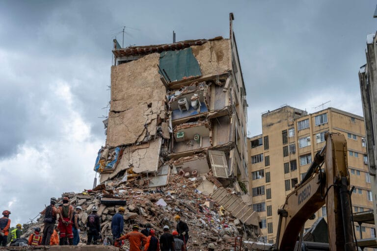 Collapsed high rise with exposed rooms and rescuers surveying rubble after a building collapse