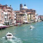 Venice canal with pastel buildings water taxis and a bright blue sky along a busy waterfront