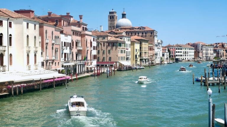 Venice canal with pastel buildings water taxis and a bright blue sky along a busy waterfront