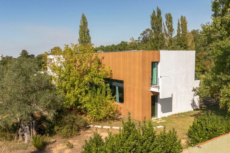 Modern white and wood clad house with a small balcony surrounded by trees on a sunny day