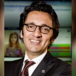 Smiling man in a dark suit and red tie wearing black glasses in a professional setting