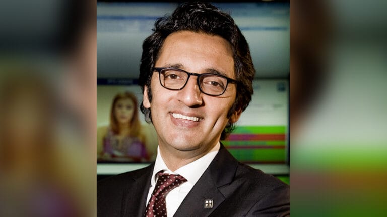 Smiling man in a dark suit and red tie wearing black glasses in a professional setting